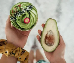 a person holding a cupcake and an avocado